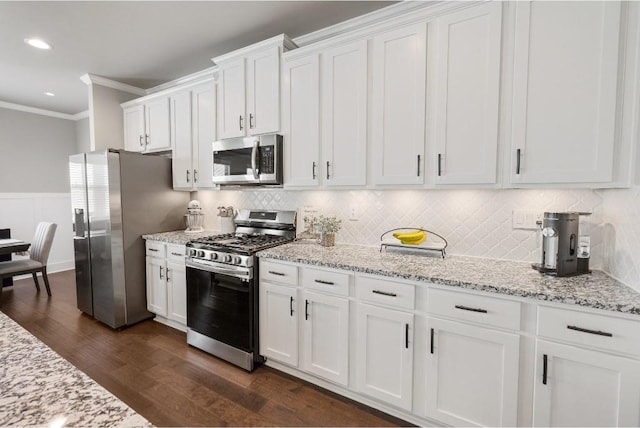 kitchen with white cabinets, wainscoting, dark wood-style flooring, stainless steel appliances, and crown molding