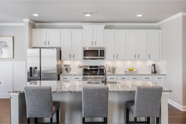 kitchen with stainless steel appliances, a sink, white cabinetry, an island with sink, and crown molding