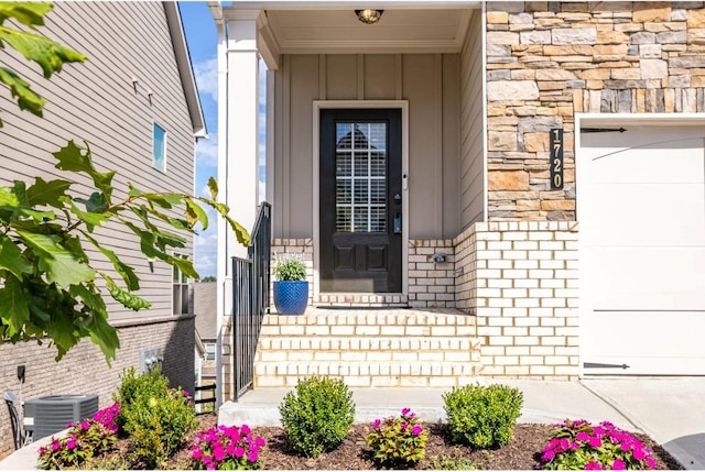 doorway to property with brick siding, board and batten siding, a garage, cooling unit, and stone siding