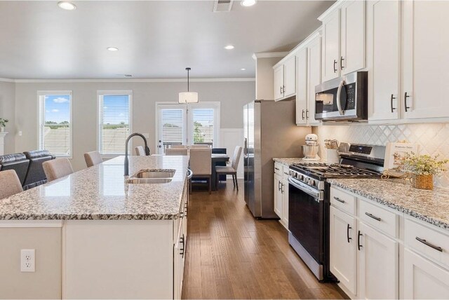 kitchen with an island with sink, dark wood-style flooring, stainless steel appliances, white cabinetry, and a sink