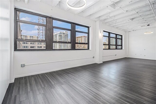 unfurnished room featuring baseboards, a city view, and dark wood-style flooring