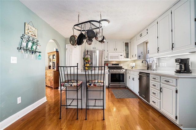 kitchen with baseboards, stainless steel appliances, wood finished floors, and white cabinets