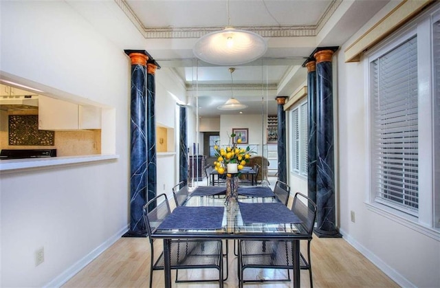 dining room featuring light wood-type flooring, ornate columns, a tray ceiling, and crown molding