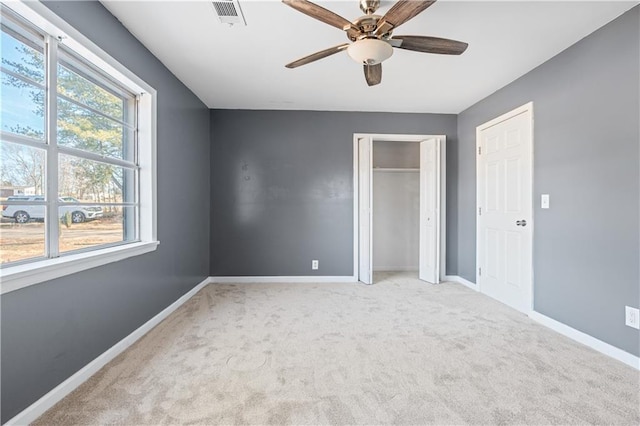 unfurnished bedroom featuring multiple closets, light colored carpet, and ceiling fan