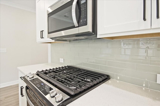 kitchen featuring light wood-style flooring, tasteful backsplash, appliances with stainless steel finishes, white cabinets, and baseboards