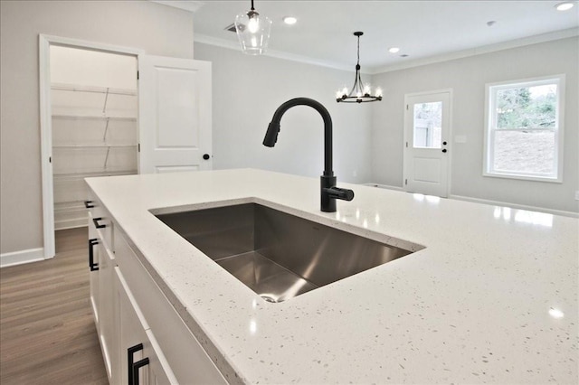 kitchen with ornamental molding, a sink, decorative light fixtures, wood finished floors, and light stone countertops