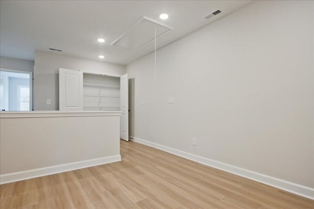 spare room featuring light wood-style floors, attic access, baseboards, and visible vents