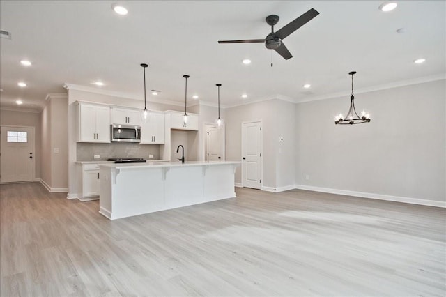 kitchen featuring stainless steel microwave, a center island with sink, decorative backsplash, white cabinetry, and a sink