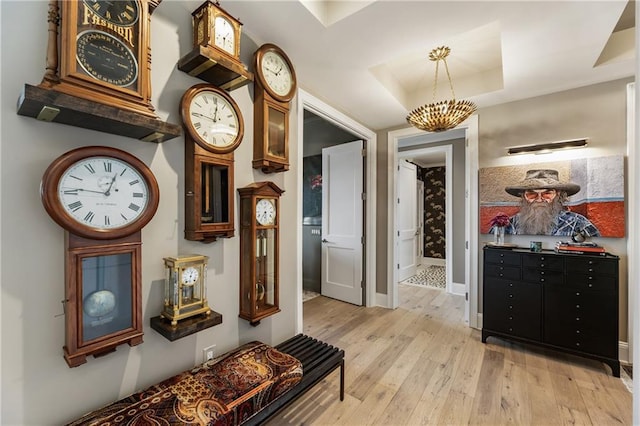 corridor featuring a tray ceiling, light wood finished floors, baseboards, and a chandelier