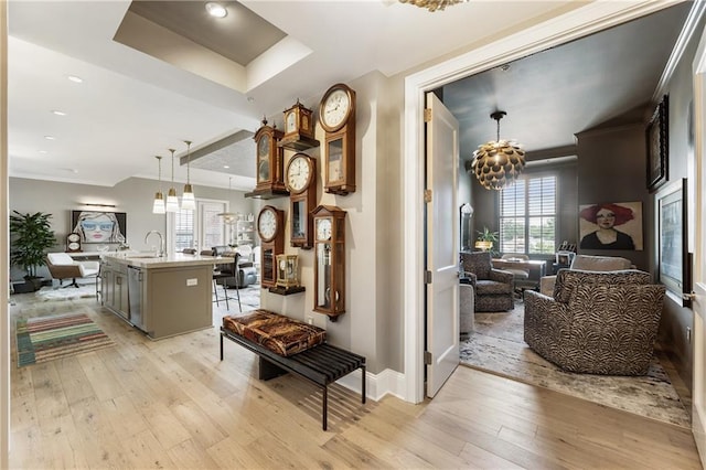 hallway featuring light wood-style floors, a tray ceiling, a chandelier, baseboards, and recessed lighting