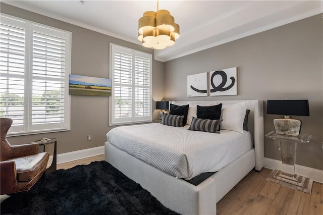 bedroom with a chandelier, wood finished floors, multiple windows, baseboards, and crown molding