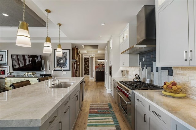 kitchen with wall chimney range hood, stainless steel range, a sink, light wood-style flooring, and recessed lighting