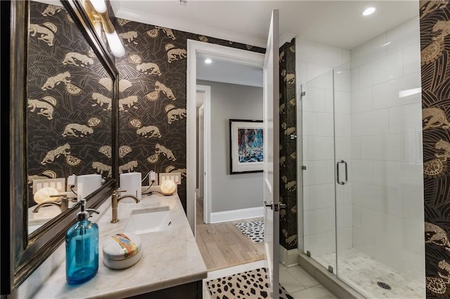bathroom with wallpapered walls, baseboards, a shower stall, crown molding, and double vanity