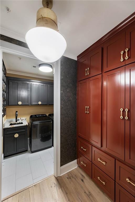 laundry room featuring washing machine and clothes dryer, ornamental molding, cabinet space, light wood finished floors, and baseboards