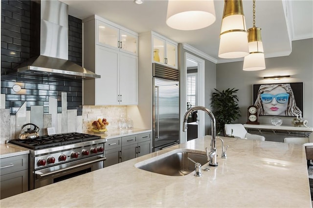 kitchen with wall chimney range hood, premium appliances, light stone counters, crown molding, and tasteful backsplash