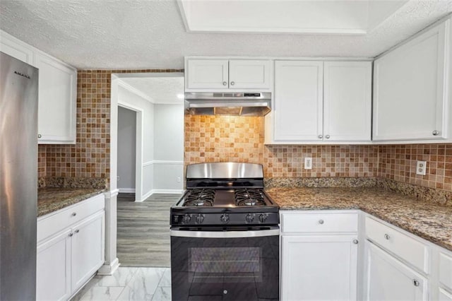 kitchen featuring freestanding refrigerator, marble finish floor, under cabinet range hood, white cabinetry, and gas stove