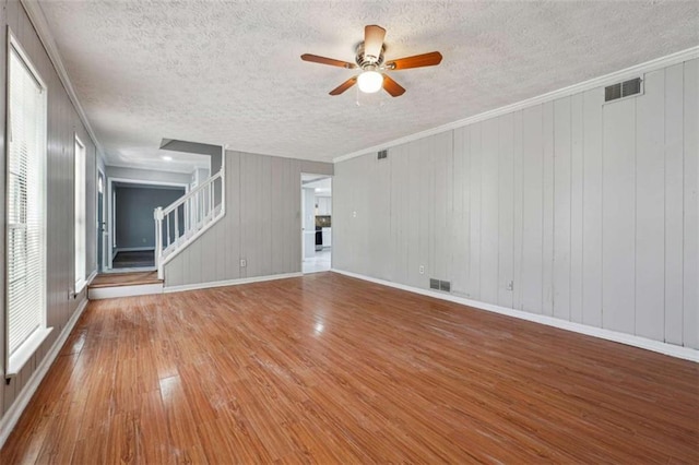 unfurnished living room featuring stairway, wood finished floors, visible vents, and crown molding