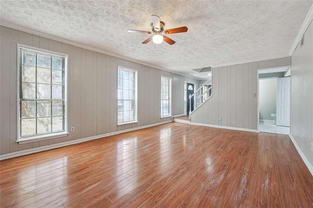 unfurnished living room featuring a textured ceiling, wood finished floors, baseboards, stairs, and ornamental molding