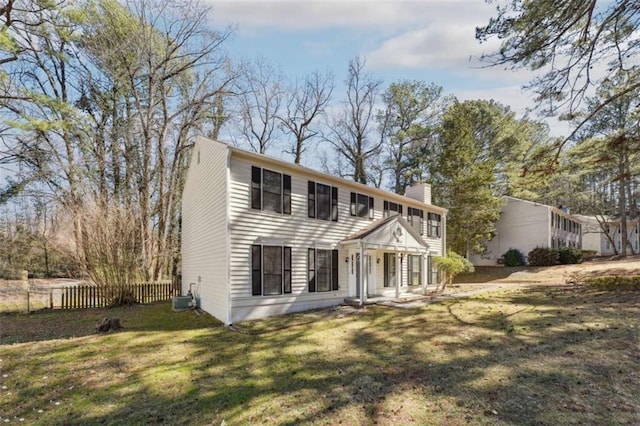 colonial home with central AC unit, a chimney, fence, and a front lawn