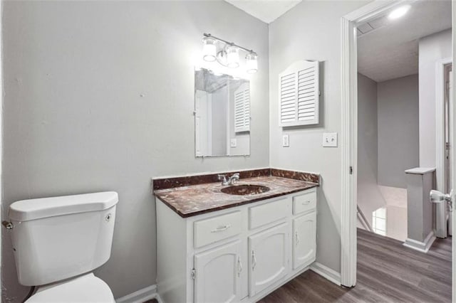 bathroom featuring baseboards, vanity, toilet, and wood finished floors