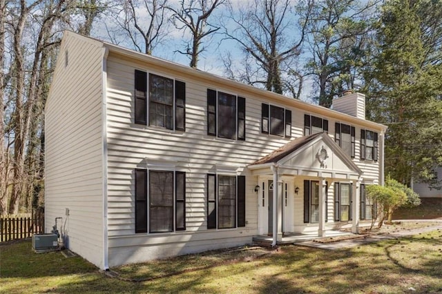 colonial-style house featuring covered porch, a chimney, fence, and a front lawn