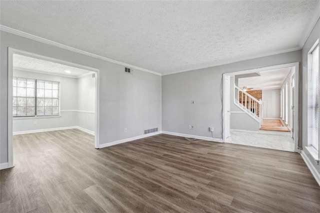 empty room featuring stairs, wood finished floors, visible vents, and crown molding