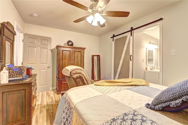 bedroom featuring light wood-type flooring, ensuite bath, ceiling fan, and a barn door