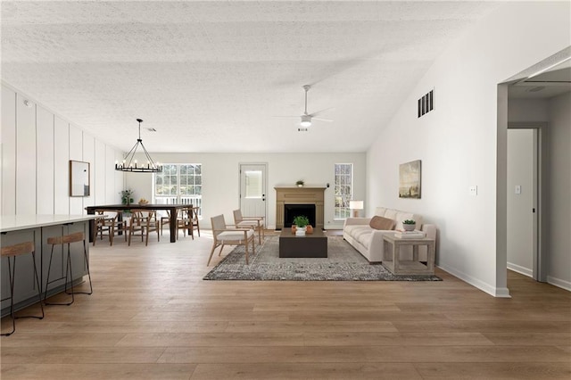 living room featuring a textured ceiling, ceiling fan with notable chandelier, lofted ceiling, and hardwood / wood-style flooring