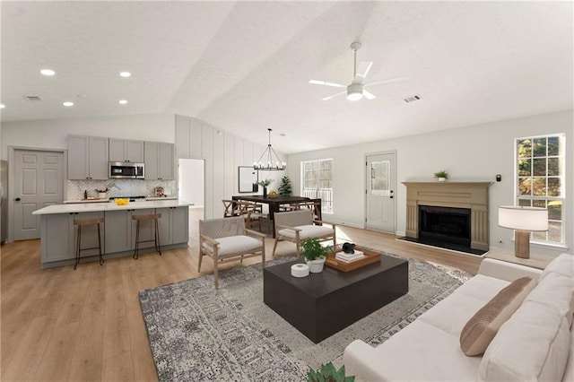 living room with vaulted ceiling, light hardwood / wood-style flooring, and ceiling fan with notable chandelier