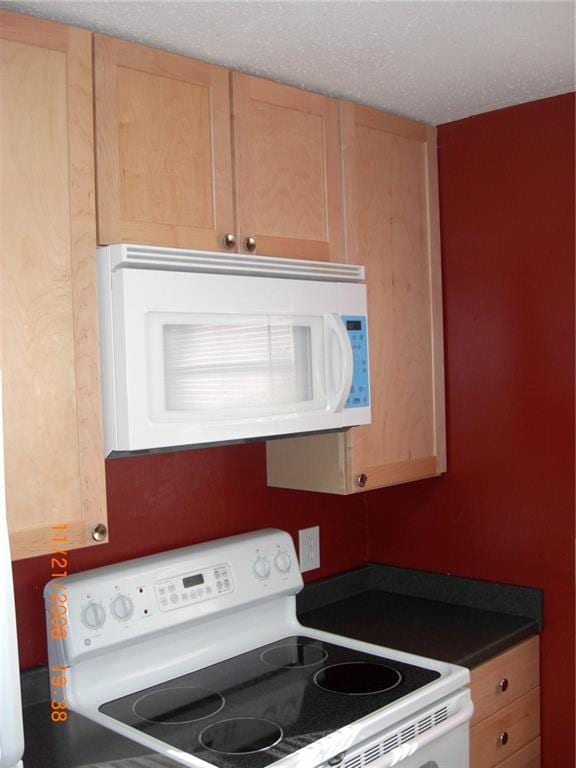 kitchen featuring white appliances, a textured ceiling, and light brown cabinets