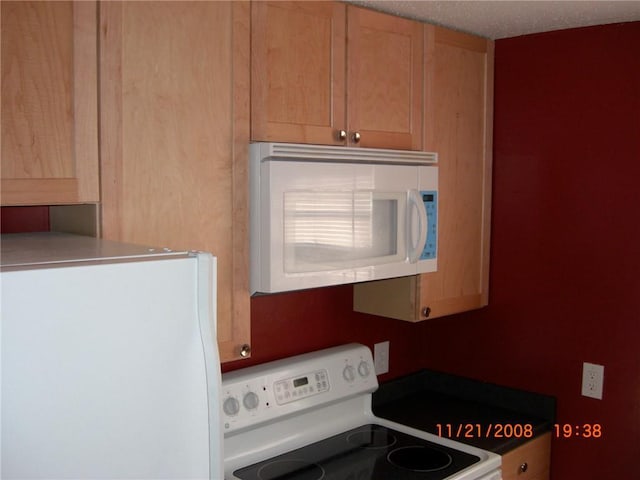 kitchen featuring light brown cabinetry, white appliances, and a textured ceiling