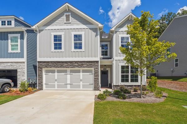 view of front of home with a front lawn, stone siding, concrete driveway, an attached garage, and board and batten siding