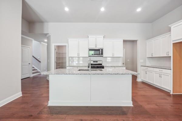 kitchen with white cabinetry, appliances with stainless steel finishes, dark hardwood / wood-style floors, light stone countertops, and decorative backsplash