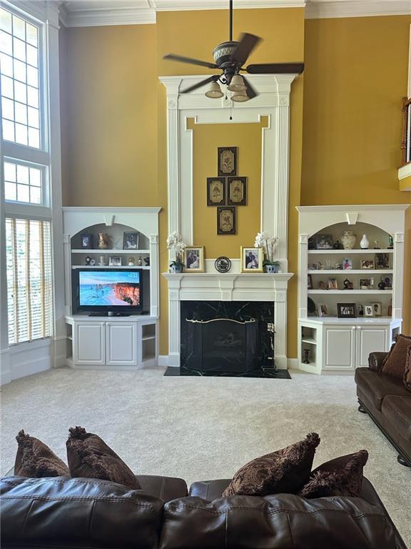 carpeted living room featuring built in shelves, ceiling fan, a fireplace, and ornamental molding