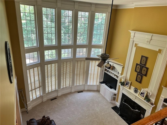 interior space with ceiling fan, light colored carpet, a fireplace, and crown molding