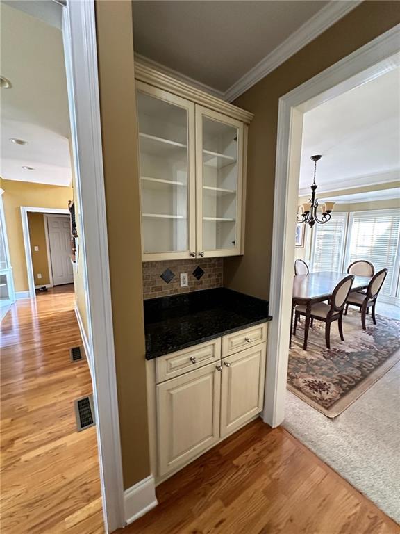 bar featuring cream cabinets, crown molding, light hardwood / wood-style flooring, decorative backsplash, and a notable chandelier