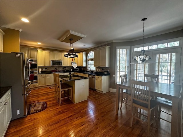 kitchen with a center island, sink, stainless steel appliances, decorative light fixtures, and a breakfast bar