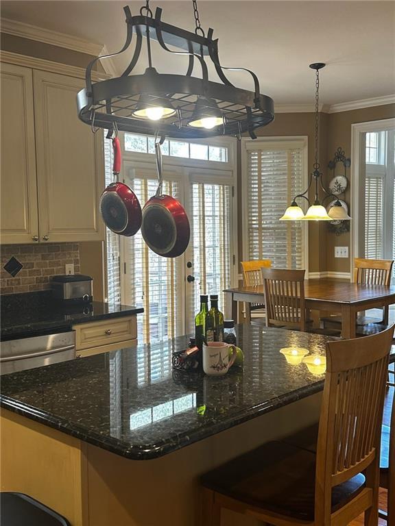 kitchen featuring pendant lighting, dark stone countertops, ornamental molding, and backsplash