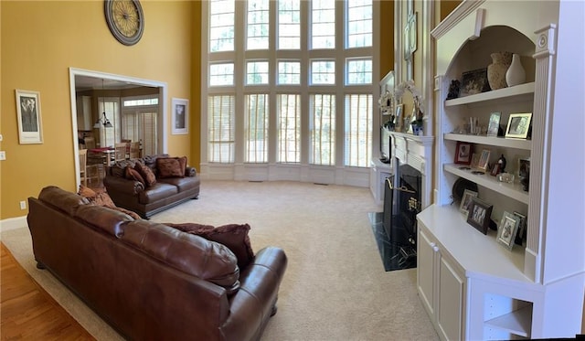 carpeted living room featuring a high ceiling, built in features, and a premium fireplace