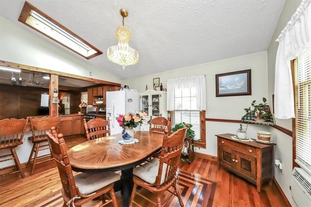 dining area with a chandelier, vaulted ceiling, a textured ceiling, and light hardwood / wood-style floors