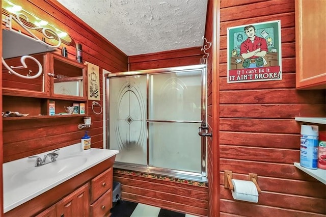 bathroom with vanity, walk in shower, a textured ceiling, and wooden walls