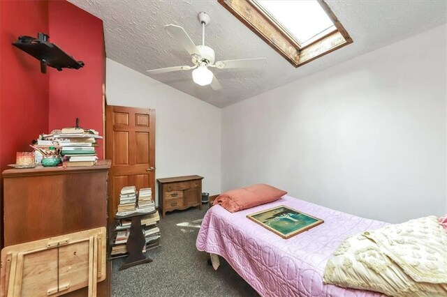 bedroom with vaulted ceiling with skylight, a textured ceiling, dark carpet, and ceiling fan