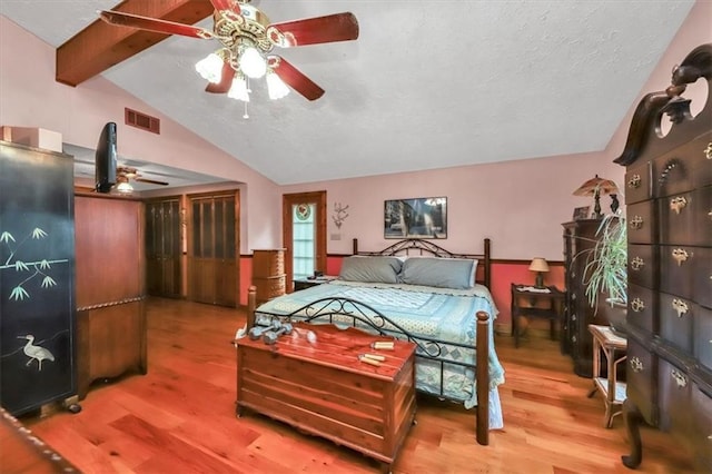 bedroom with lofted ceiling with beams, a textured ceiling, wood finished floors, and visible vents