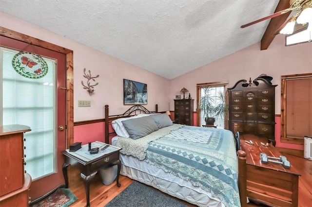 bedroom featuring lofted ceiling with beams, ceiling fan, a textured ceiling, and wood finished floors