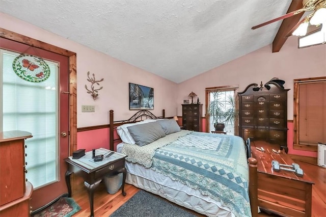 bedroom featuring ceiling fan, wood-type flooring, a textured ceiling, and vaulted ceiling with beams