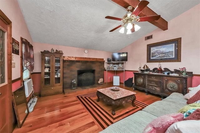 living room featuring vaulted ceiling with beams, a textured ceiling, visible vents, and wood finished floors