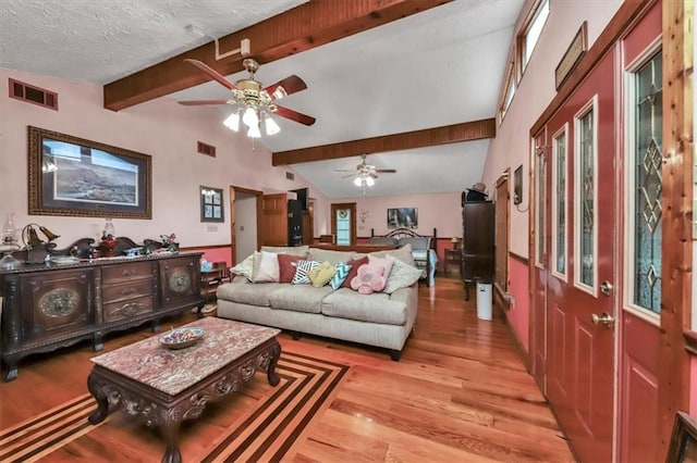 living room featuring vaulted ceiling with beams, light wood-type flooring, visible vents, and a textured ceiling