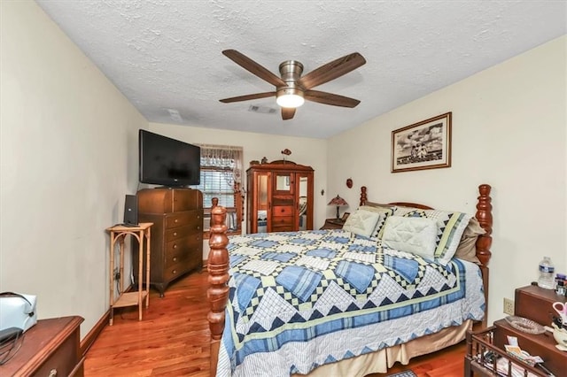 bedroom with a textured ceiling, wood-type flooring, and ceiling fan