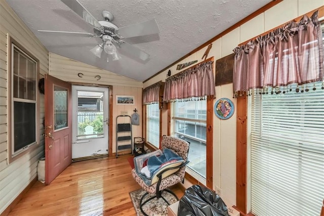 sitting room with wooden walls, a ceiling fan, light wood-style flooring, vaulted ceiling, and a textured ceiling