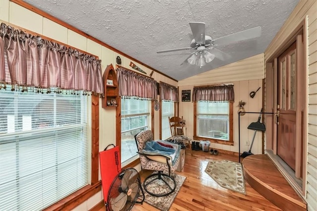 living area with ornamental molding, a ceiling fan, vaulted ceiling, a textured ceiling, and wood finished floors